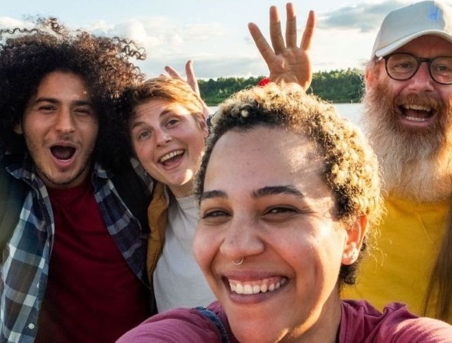 A woman in the foreground takes a selfie with three smiling friends in the background