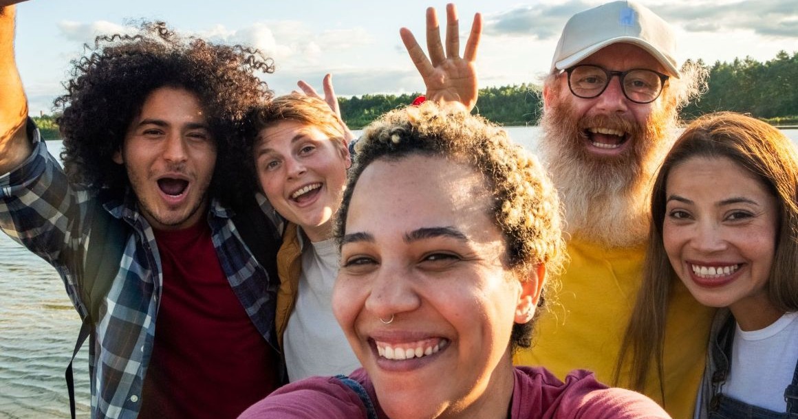 A woman in the foreground takes a selfie with three smiling friends in the background
