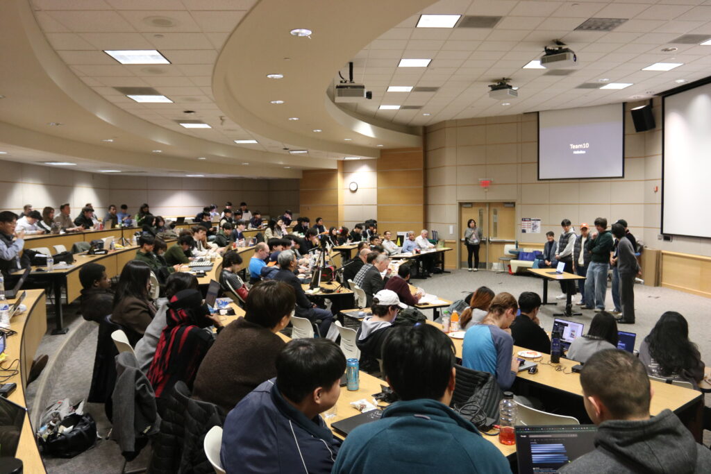 A large classroom with people looks at a group of people at the front of the room.