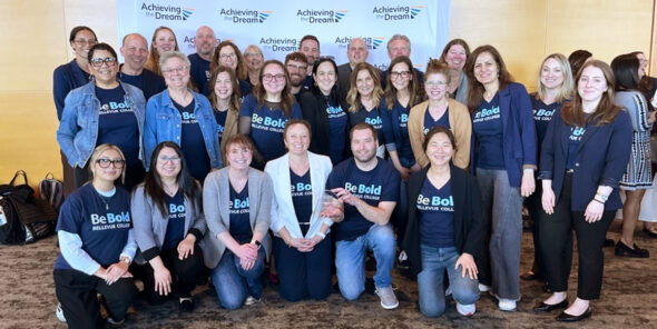 Large group of people stand in front of Achieving the Dream step and repeat.