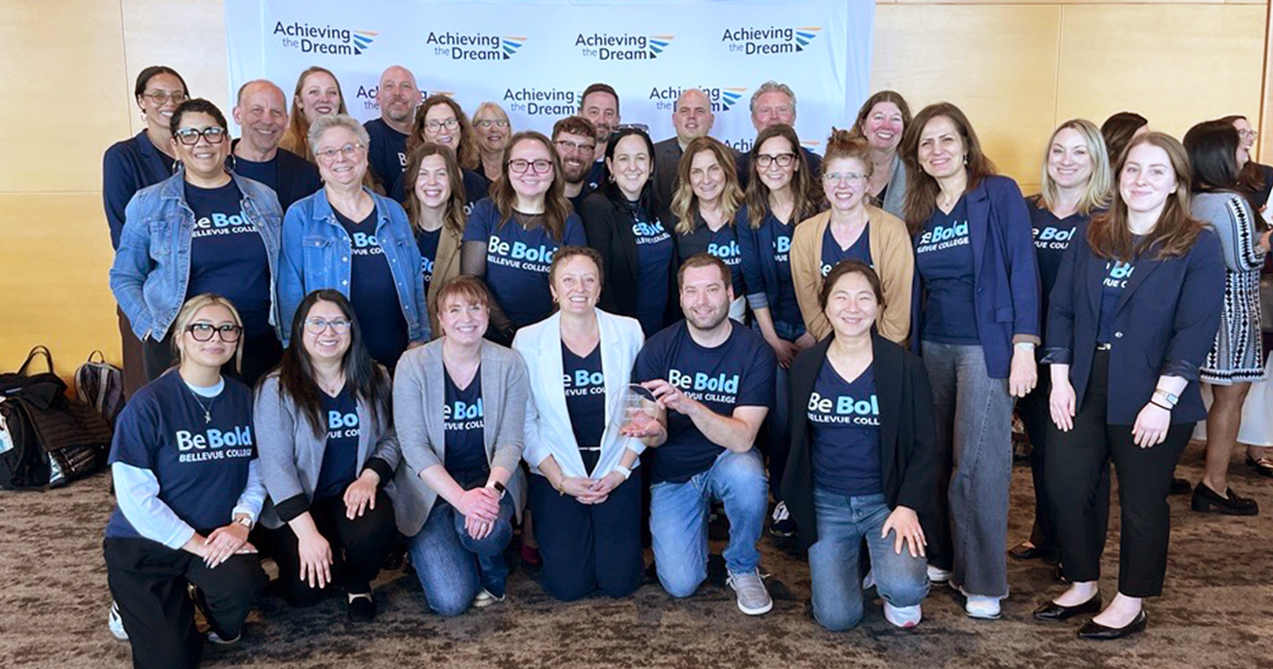 Large group of people stand in front of Achieving the Dream step and repeat.