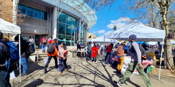 People walk outside on campus near C Building with white tents up.