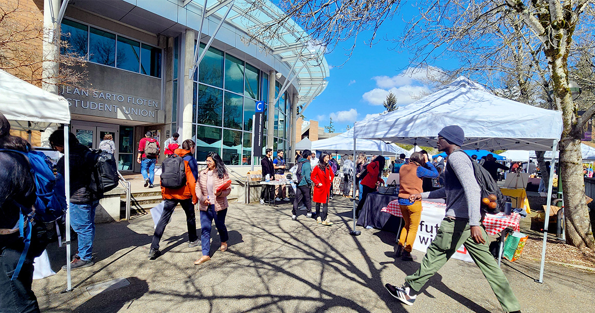 People walk outside on campus near C Building with white tents up.