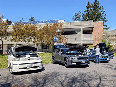 Three electric vehicles outside with their hoods up.