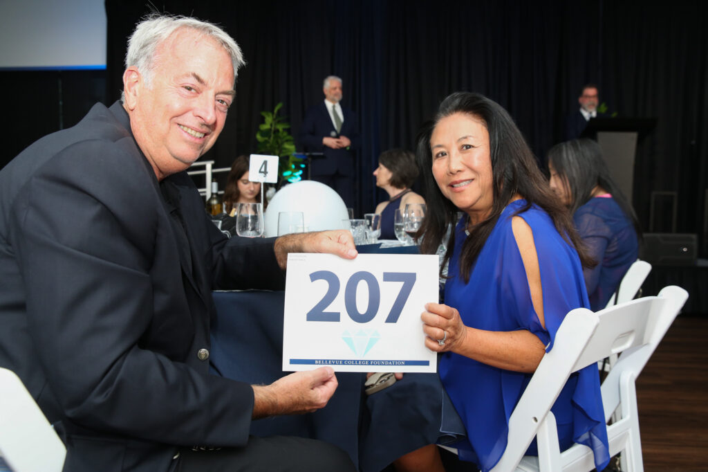 Two people hold up their bidding number while sitting at a table at the Diamond Jubilee.