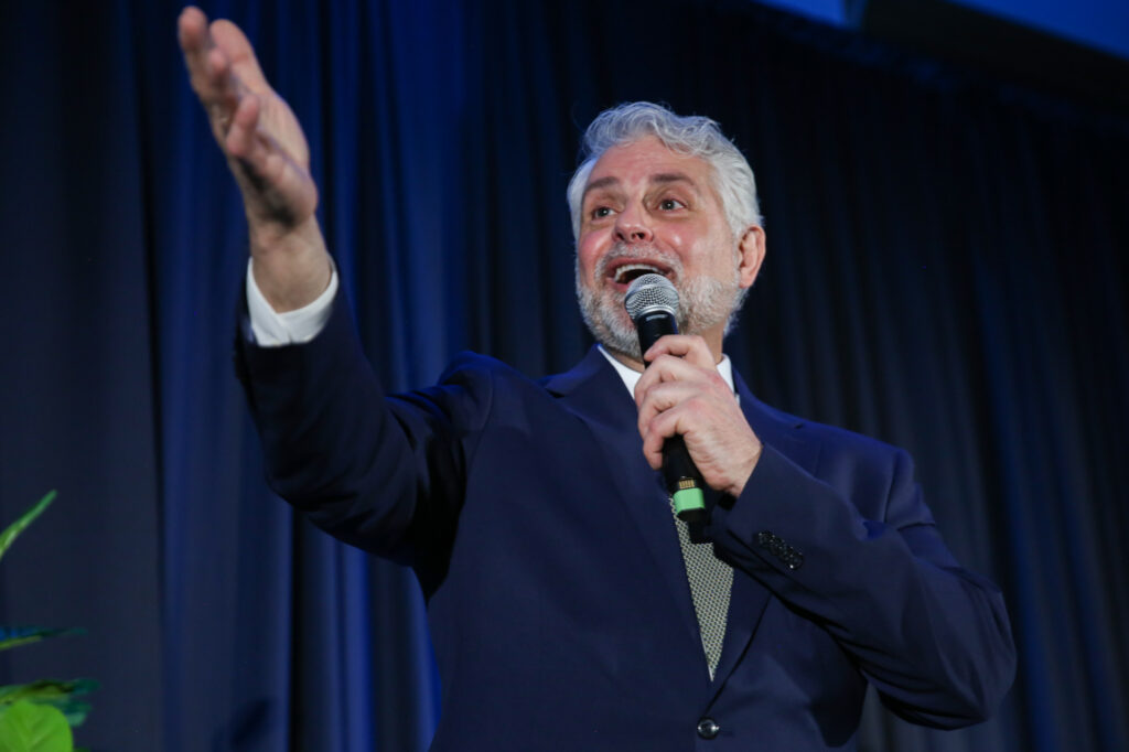 Auctioneer raises his hand as he speaks on stage.