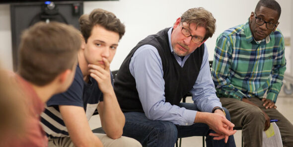 Three people sitting look toward one person looking back at them.