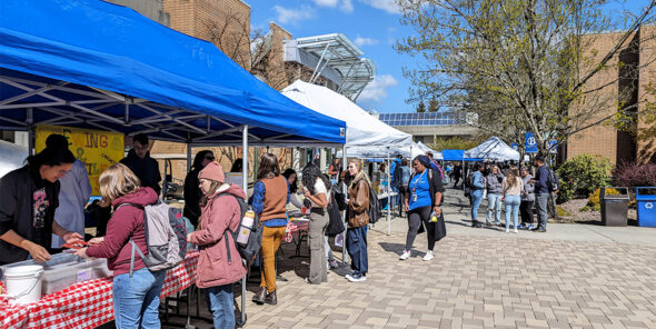 Students outside on campus standing at tables under tents.