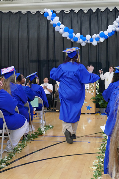 Graduate dressed in blue regalia walks down the aisle at a commencement ceremony.