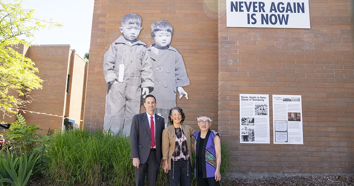 Bellevue College President David May, artist Erin Shigaki, and activist Stan Shikuma stand in front of the Never Again is Now mural on the Bellevue College campus.