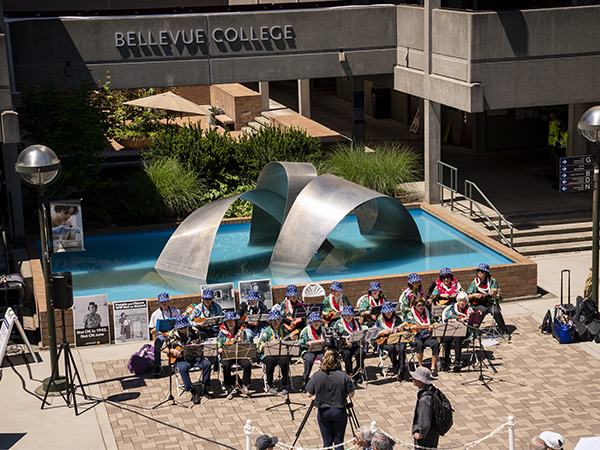 Ukulele players sit in front of the Bellevue College fountain.