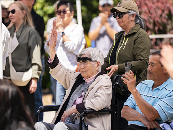 Sitting guest raises hand in crowd at the Never Again is Now mural ceremony.