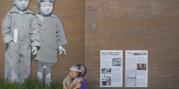 Two people hug in front of the Never Again is Now mural on Bellevue College's campus.