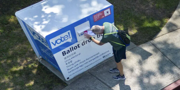A person puts a ballot into a ballot drop box outside.