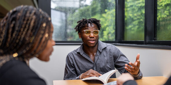 Two students sit at the table. One has a book open.
