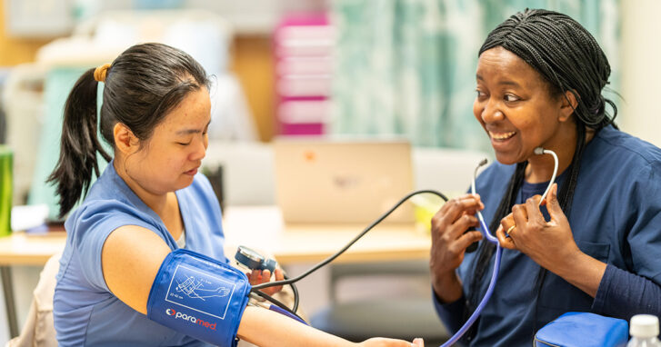 One student takes the blood pressure of another student.