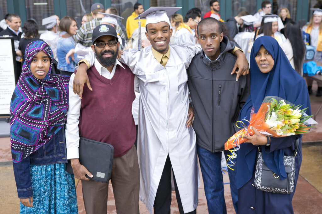 A graduatein cap and gown proudly poses with his family.