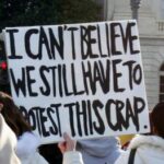 Protesters holding a sign that reads "I can't believe we still have to protest this crap."