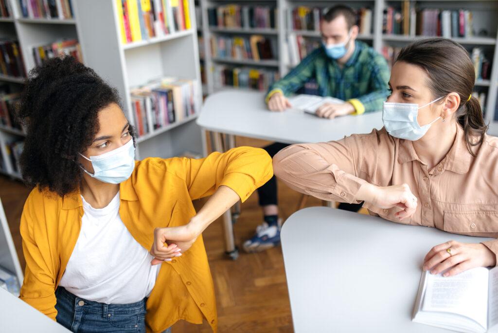 Two masked students doing a elbow bump in class