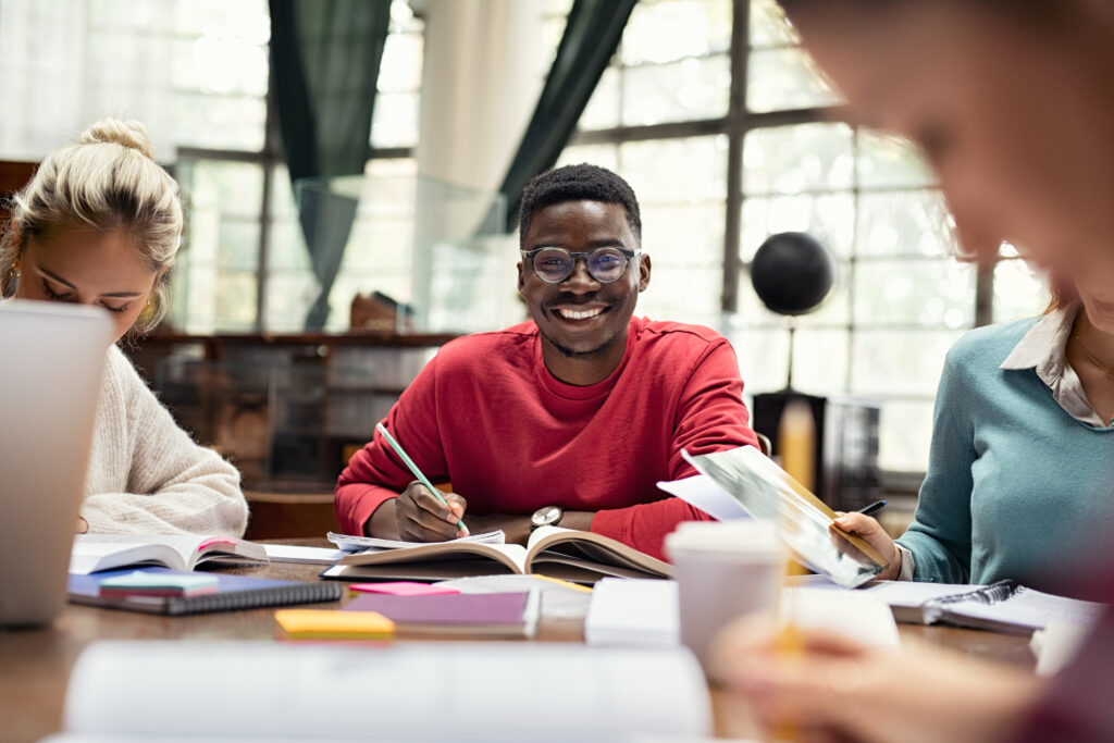 Portrait of smiling black student in library with classmates studying.