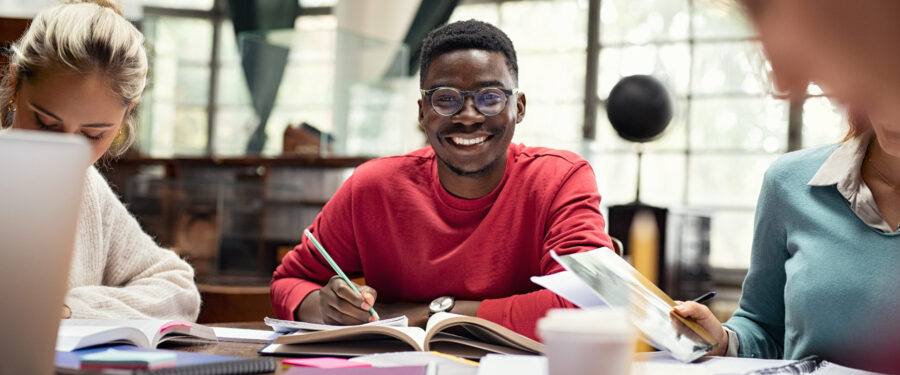 Portrait of smiling black student in library with classmates studying.