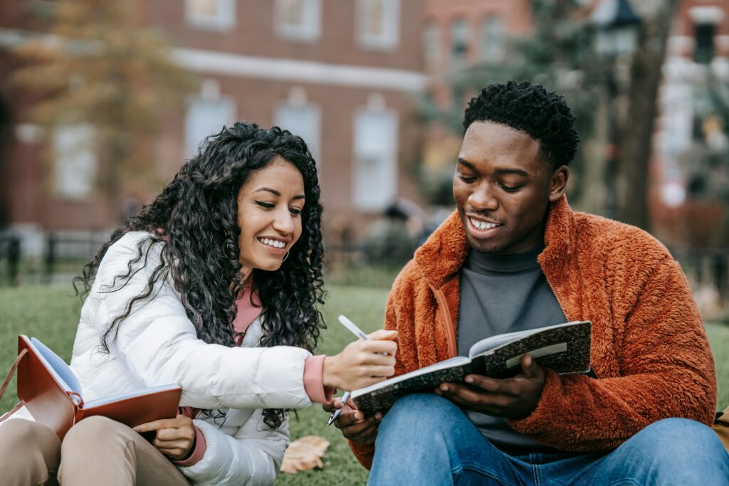 A woman with brown skin and long black curly hair collaborating with a young black man with notebook in hand.