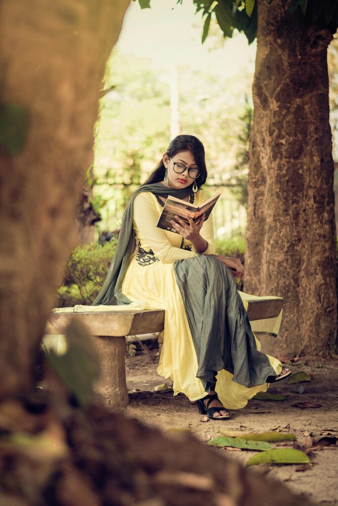Dark haired woman in sari reading a book under trees