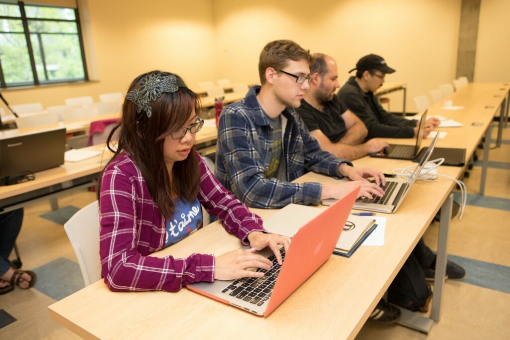 Four CS students work on their laptops in a classroom.