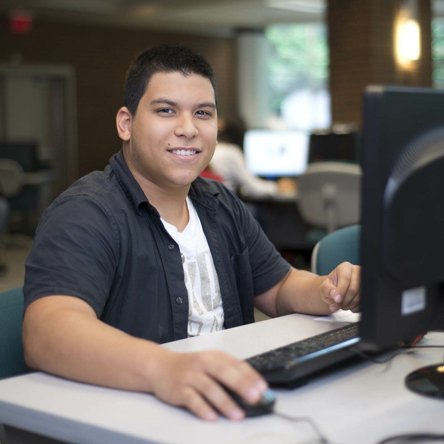 A student sitting in front of a computer smiles at the camera.