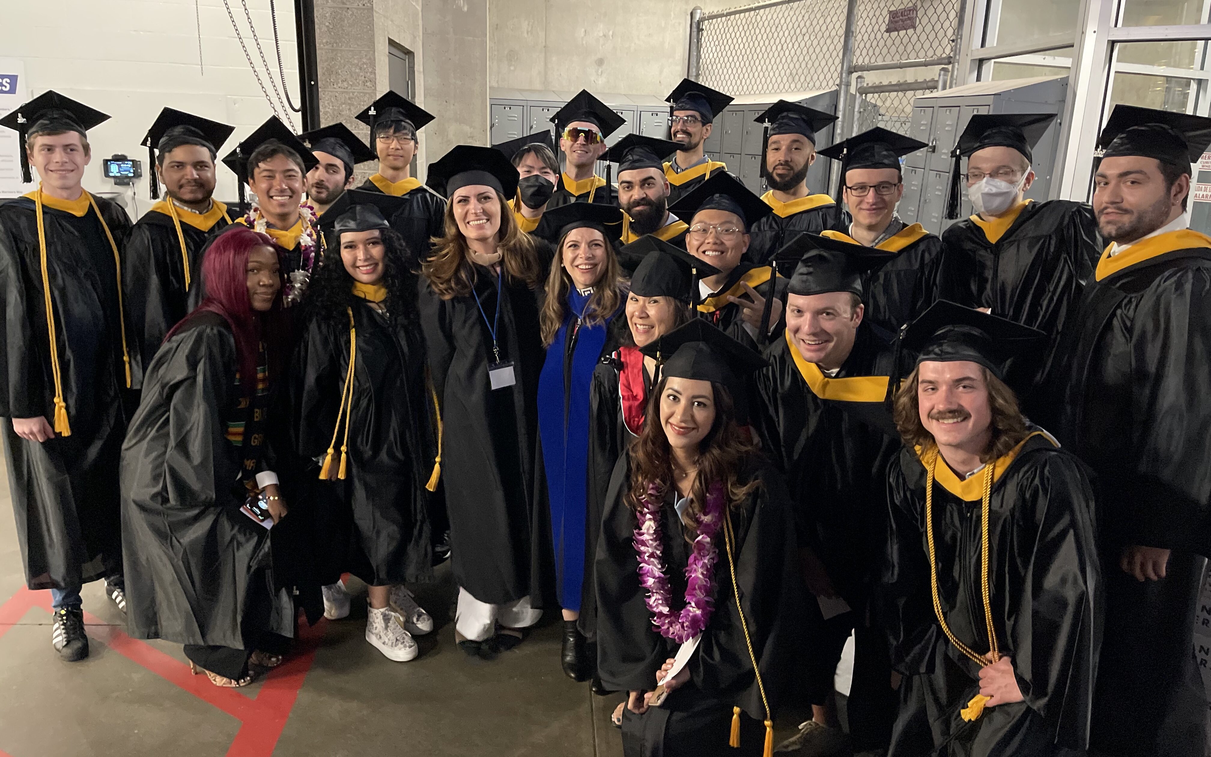 19 graduates from the BS in Computer Science program pose with three faculty and staff members from the program at Bellevue College's 2022 graduation. All smile at the camera while wearing graduation regalia.