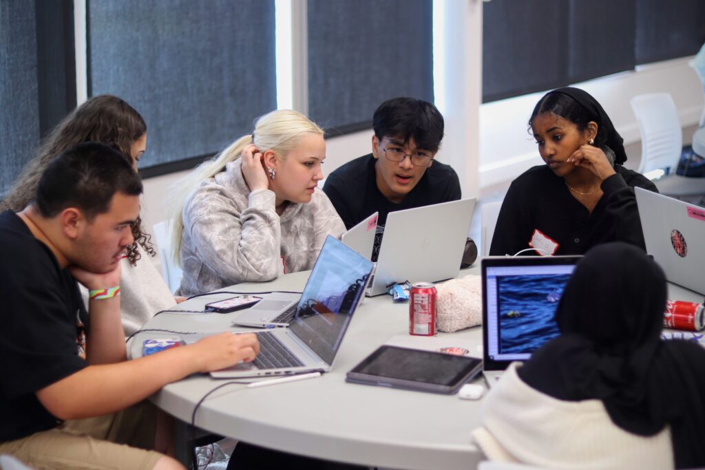 A group of student huddled around a laptop at the CodeDay hackathon event.