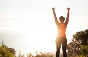 Woman in workout clothes with hands up at sun rise.