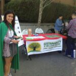 woman in green cape standing next to Sustainability Departments desk while student registers