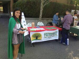 woman in green cape standing next to Sustainability Departments desk while student registers