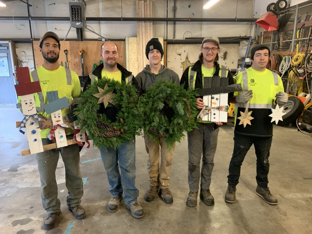 Grounds Crew holding crafts (wooden snowperson, wreaths, and wooden stars) made at the Winter Holiday Crafting Event.