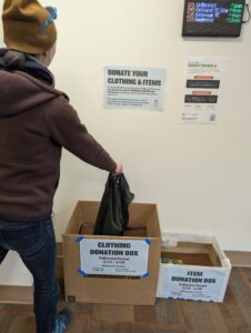 Student employee dropping off clothes in the donation drive cardboard box.