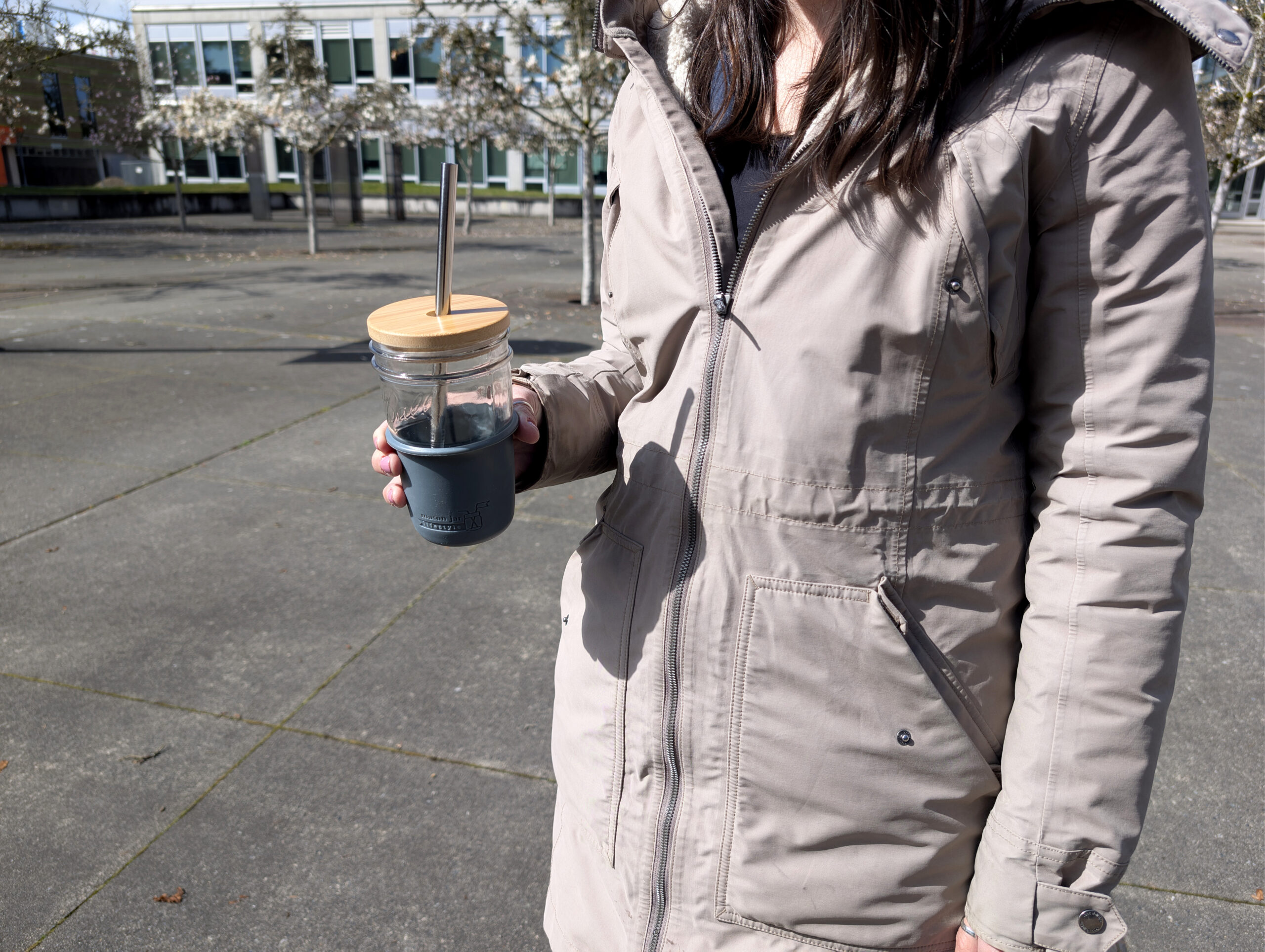 Employee in tan jacket holding glass mason jar with straw