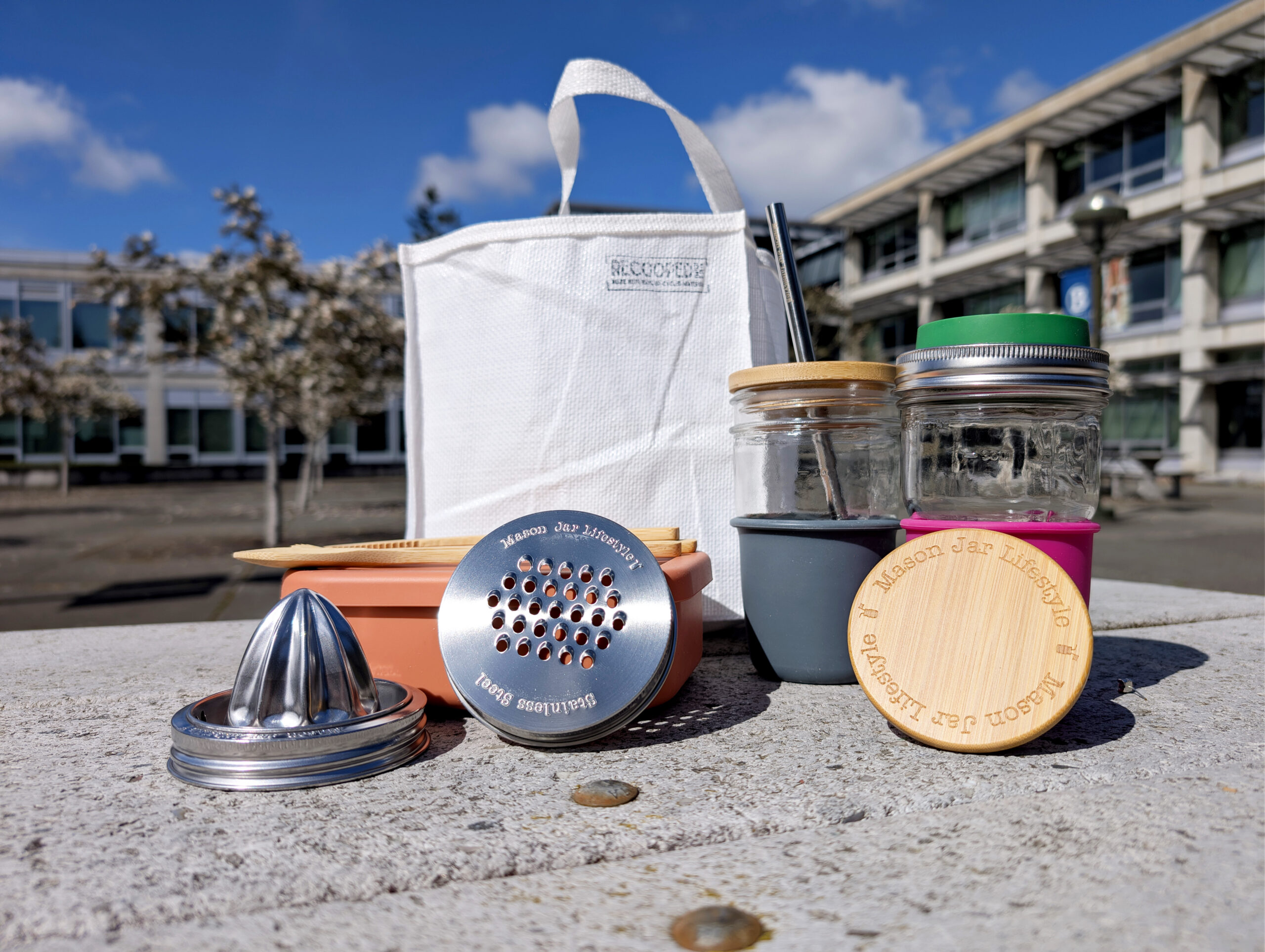 list of earth month prizes which is a white reusable bag, various mason jars and lids and a lunch box on a table outside