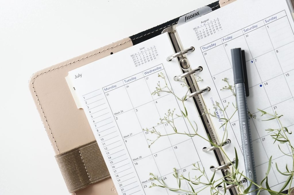 Close view of a planner calendar with a pen and a sprig of green plant