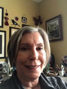 Sue Clary close-up with a desk and art behind her.