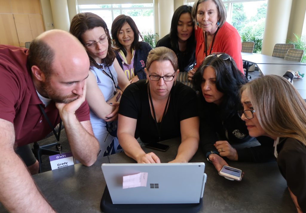 Eight people huddled around a laptop with one person typing