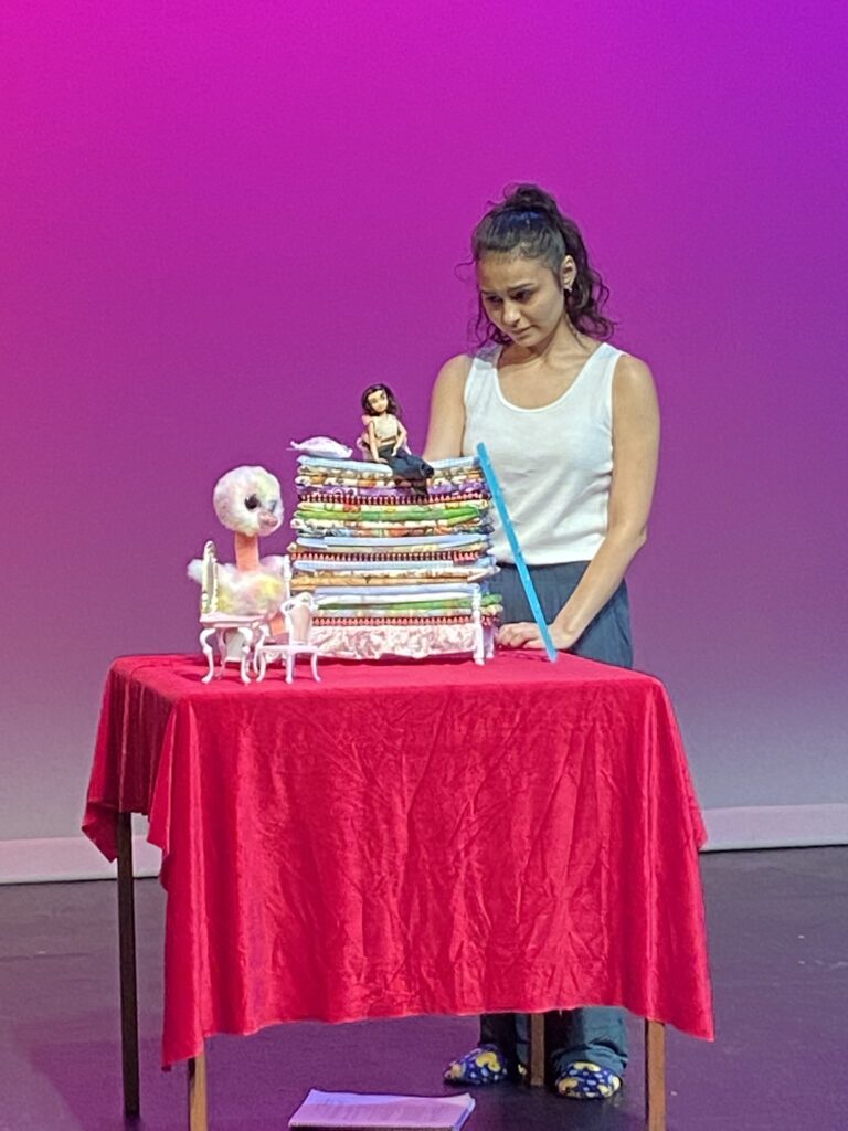 Student looking down at an doll on top of small mattresses all on a red-covered table with a purple background.