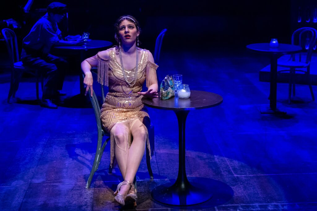 Woman sitting at small table on stage with blue background lighting