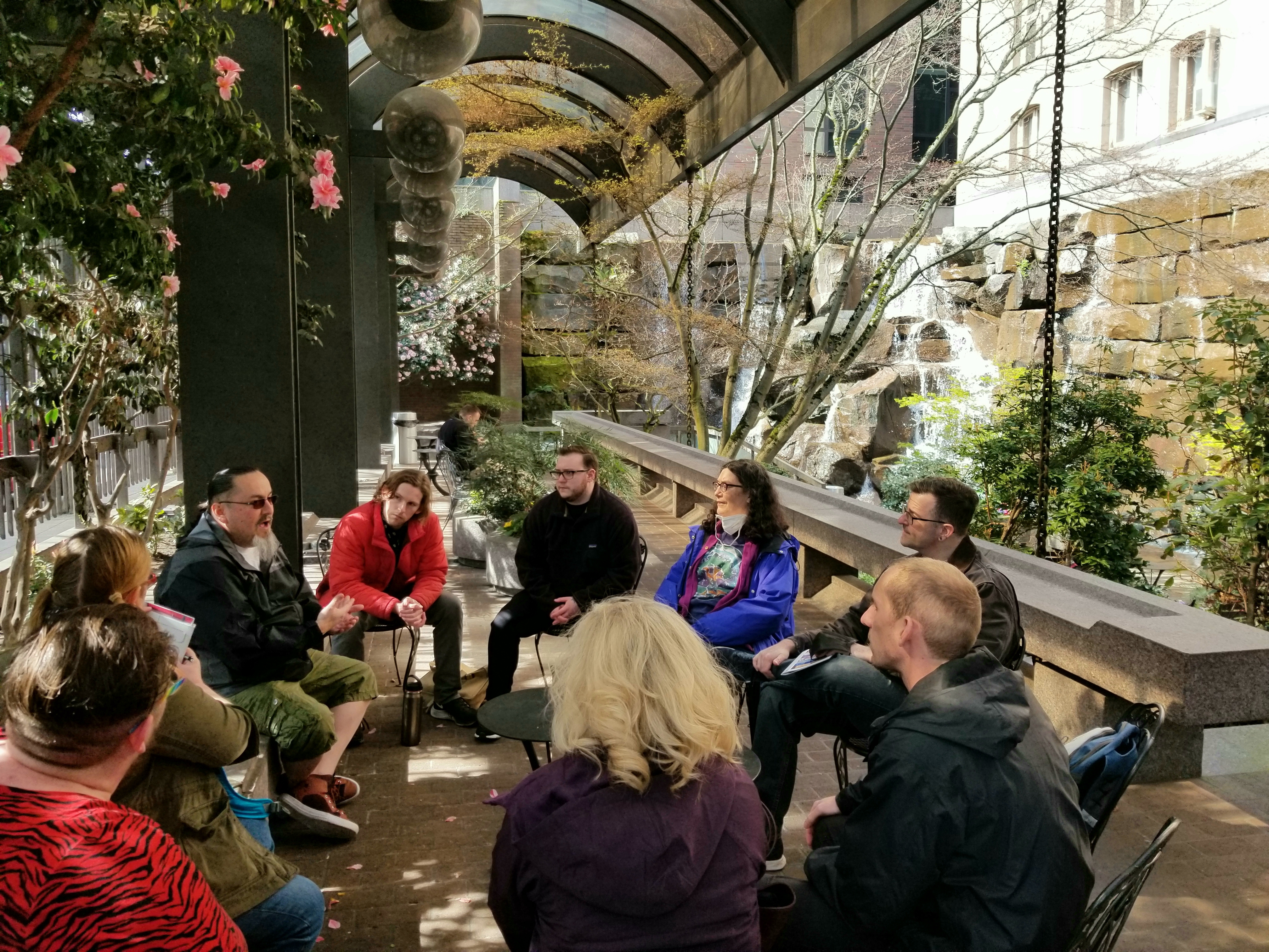 People sitting around in a circle listening to someone talking while in a park