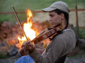 Photo of Miriam Oommen playing fiddle with campfire in background