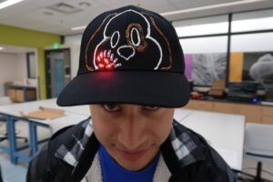 Person showing off a cap with a dog drawn on it and glowing LEDs on it