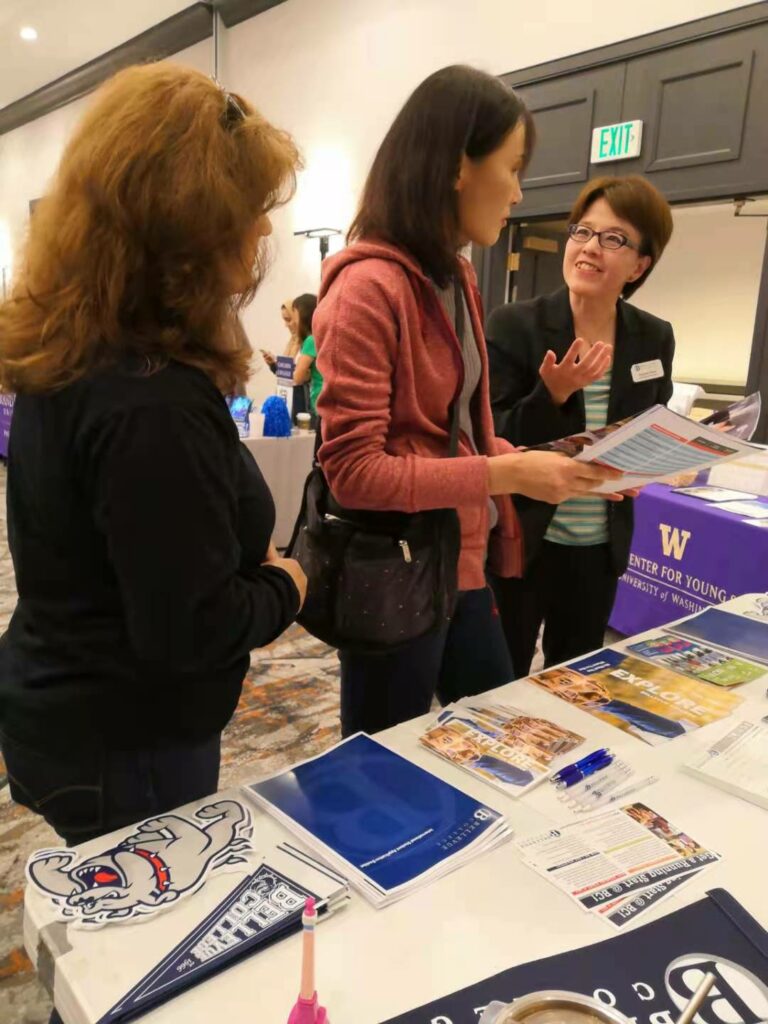 Three people holding Bellevue College brochures talking over a table at a recruitment fair.