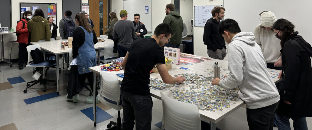 Students chatting, completing puzzles and getting snacks around two tables set up in a classroom.