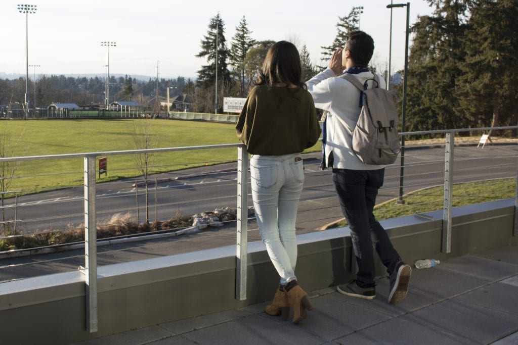 One female student and one male student leaning against a chain link fence