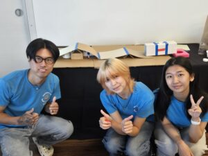Three students in BARC blue t-shirts posing after completing a putt putt golf challenge station using cardboard and tape.